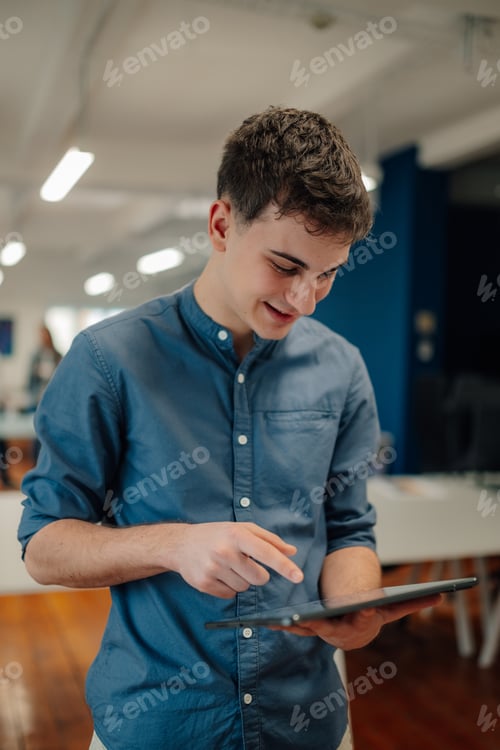 Preview: Young man using tablet in modern office, browsing internet, smiling
