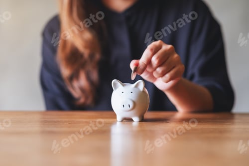 Preview: Closeup image of a woman putting coin into piggy bank for saving money concept