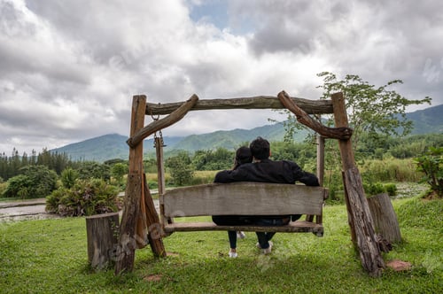 Preview: Young couple sitting on wood swing in national park