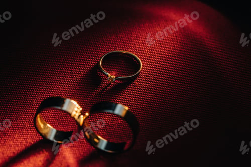 Preview: Two wedding rings and one engagement ring on a red background. three Gold rings of a couple in love
