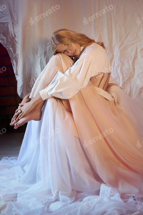 Preview: Model poses in soft fabric setting with gentle light and soft colors in studio space