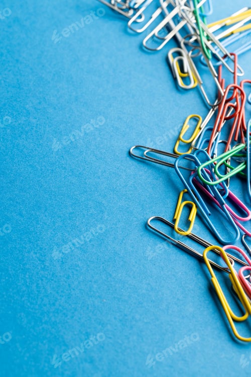 Preview: Close up of stack of multi coloured paper clips and copy space on blue background