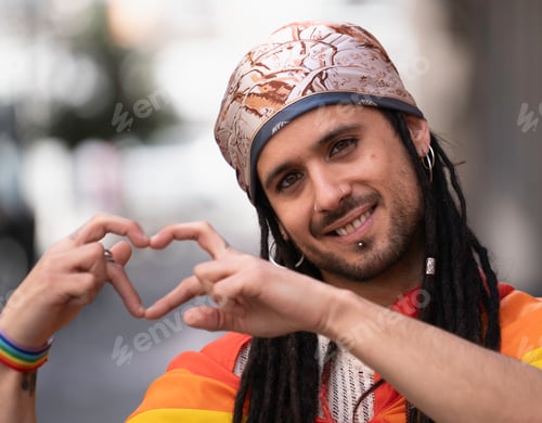 Preview: Young man showing heart symbol with hands at pride parade