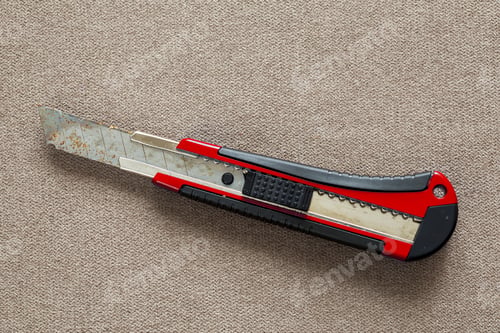 Preview: Close-up of isolated stationery retractable metallic knife with sharp blade on light cloth copy