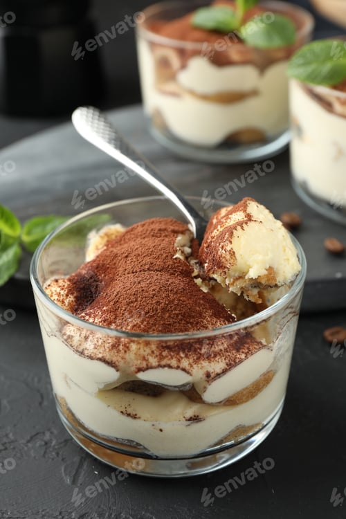 Preview: Delicious tiramisu in glasses and spoon on black table, closeup