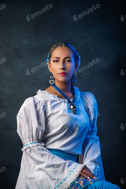 Preview: A woman wearing a white dress and blue skirt sits in front of a blue wall