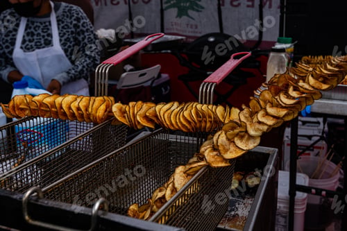 Preview: lots of potato slices on log metal skewers deep fried in street food kitchen