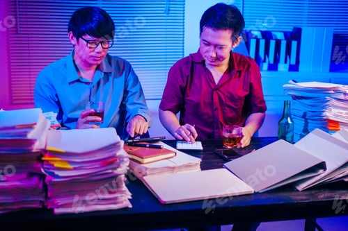 Preview: Two men are working late at office,drinking beer while checking documents.They are overwhelmed