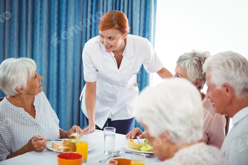 Preview: Smiling nurse looking at senior person during breakfast