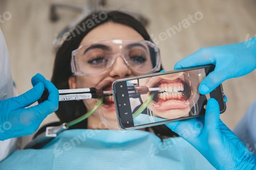 Preview: Dental care procedure at stomatology cabinet, medical assistant taking teeth photo using smartphone