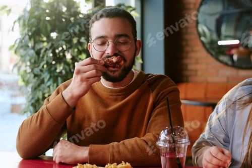 Preview: Young Adult Middle Eastern Man Enjoying Eating Fried Chicken at Restaurant Table