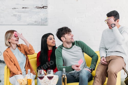 Preview: multiethnic friends having fun at home party and fixing stickers to foreheads