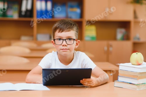 Visualização: Aluno do ensino fundamental usando tablet digital com colega estudando em segundo plano na sala de aula