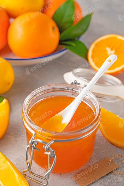 Preview: Homemade delicious orange jam with fresh oranges in a glass jar on a gray concrete background.