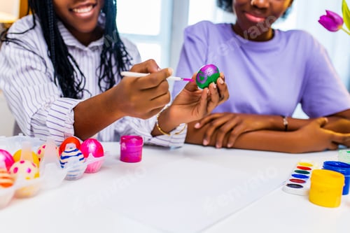 Preview: multiracial two women painting eggs with cute pink rabbit costume ears in apartment