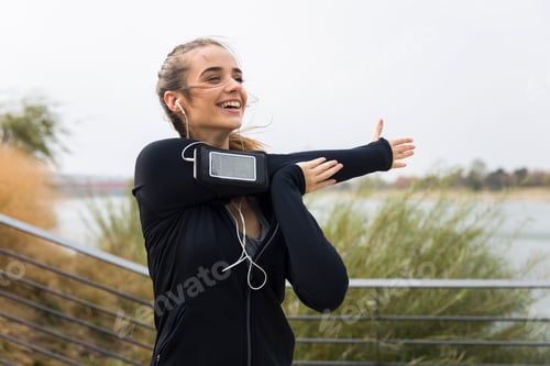 Preview: Female athlete stretching her arms while listening to music outdoors
