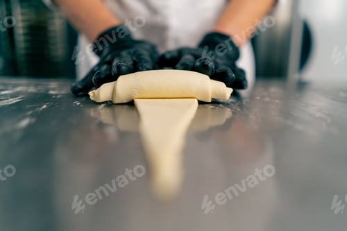 Preview: Close-up chef's gloved hands shaping and twisting raw dough into the shape of croissants for baking