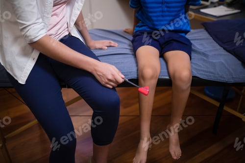 Preview: Low section of female therapist examining boy with reflex hammer on knee