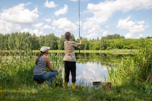 Preview: Mother and teenage son fishing together on lake shore, enjoying summer day in nature