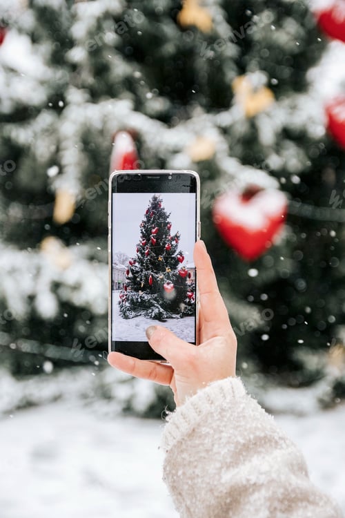Preview: Selective focus photo of hand holding mobile phone, taking photo of christmas tree.