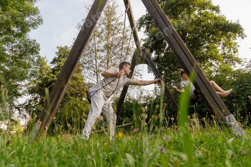 Preview: A joyful father pushes his child on a swing, both smiling and laughing.