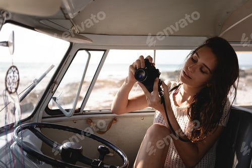Preview: Front view of beautiful Caucasian woman using digital camera in camper van at beach on a sunny day