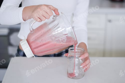 Preview: Young girl is pouring a smoothie from a blender into a mason jar glass
