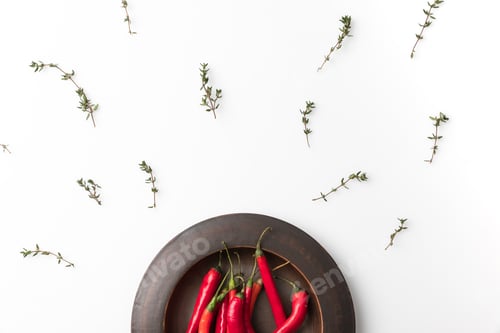 Preview: Top view of red chili peppers on black plate and twigs of thyme isolated on white