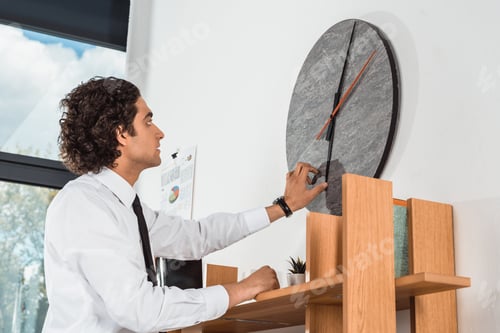Preview: side view of young businessman setting time on clock in office