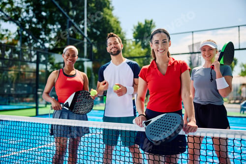 Preview: Multiracial group of athletes playing paddle tennis mixed doubles and looking at camera.