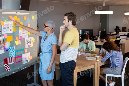 Preview: Creative business people looking at sticky notes on glass board