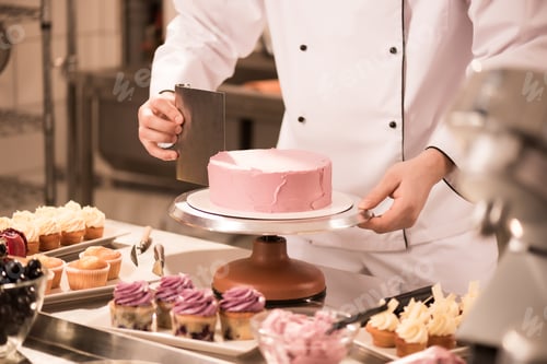 Preview: cropped shot of confectioner making cake in restaurant kitchen