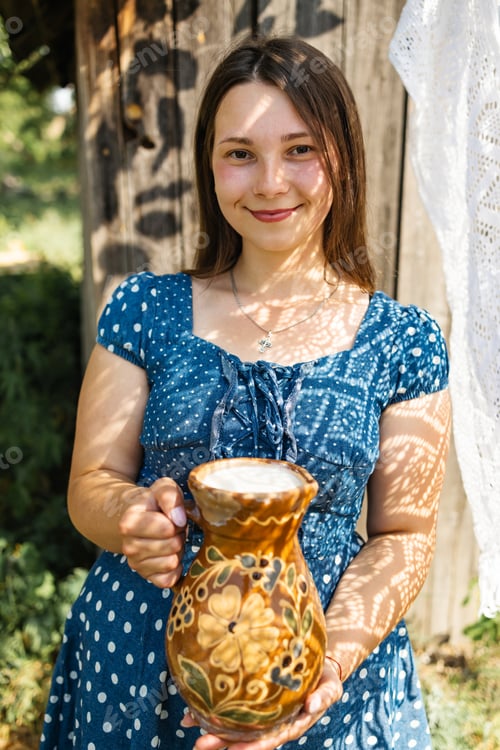 Preview: Young farmer woman smiling on camera carries jug of milk after milking cow on farm pasture. Natural