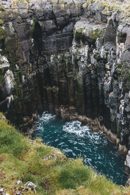 Preview: aerial view of rocky cliff and crashing blue waves in Iceland