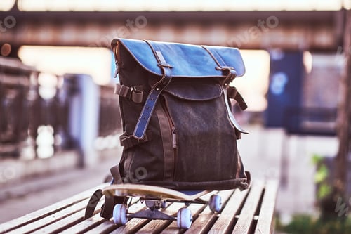 Preview: Close-up photo of a backpack lying on a skateboard that stands on a bench