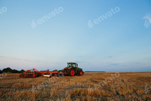 Preview: Modern tractor with a heavy trailed disc harrow works a wide hilly field.