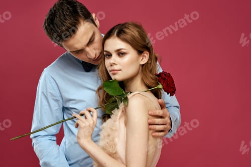 Preview: enamored man and woman with a red flower on a pink background hug each other Copy Space