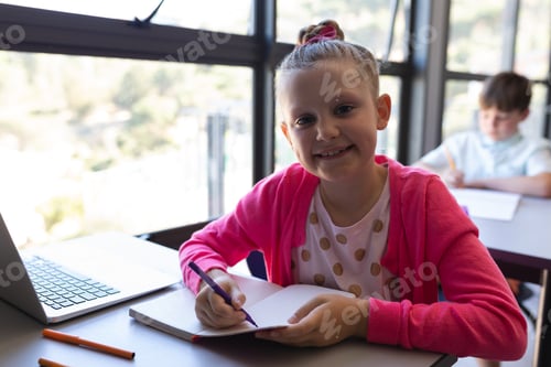 Visualização: Aluna escrevendo no caderno e olhando para a câmera na mesa na sala de aula do ensino fundamental