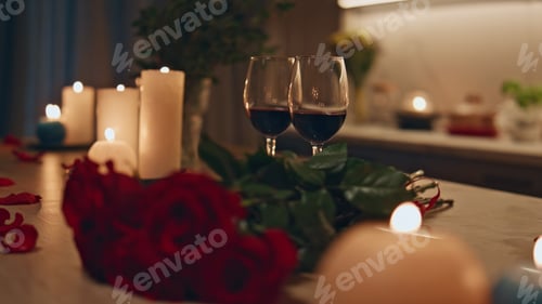 Preview: Two wine glasses standing wooden kitchen table with burning candles close up.