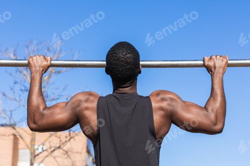 Preview: Unrecognizable strong black sportsman working out on bar in town