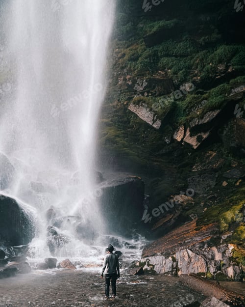 Preview: Man standing in front of a beautiful waterfall surrounded cliffs