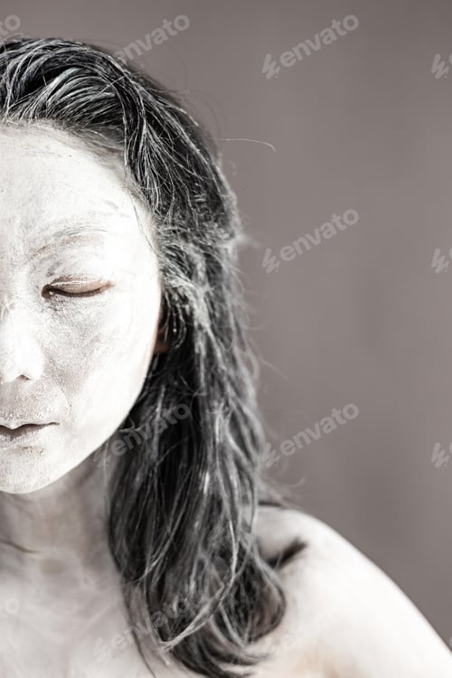 Preview: Art portrait of asian woman covered in clay isolated over grey background. Woman face like cracked p