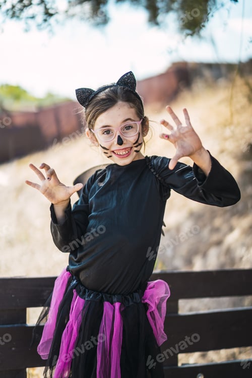 Preview: Cute little girl wearing a Halloween cat costume smiling and scaring the photographer