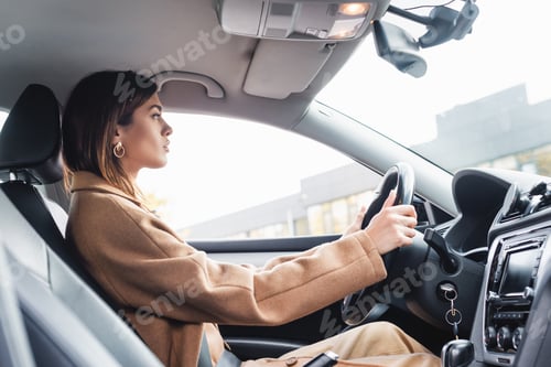 Preview: side view of woman in trench coat driving car on blurred foreground