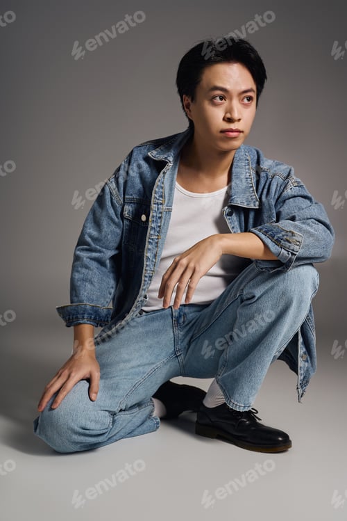 Preview: Young asian man showcases casual style in a modern grey studio setting