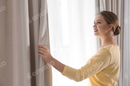 Preview: Woman opening window curtains at home in morning