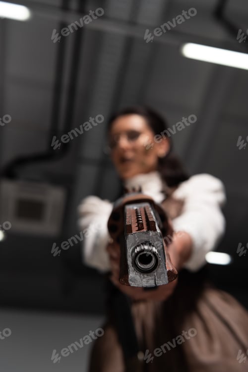 Preview: selective focus of confident steampunk woman aiming with pistol at camera