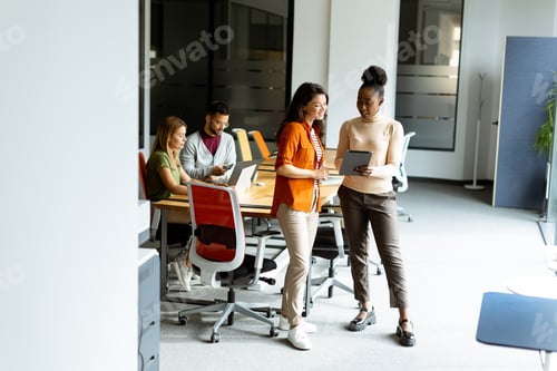 Preview: Two young business women with digital tablet in the office in front of their team