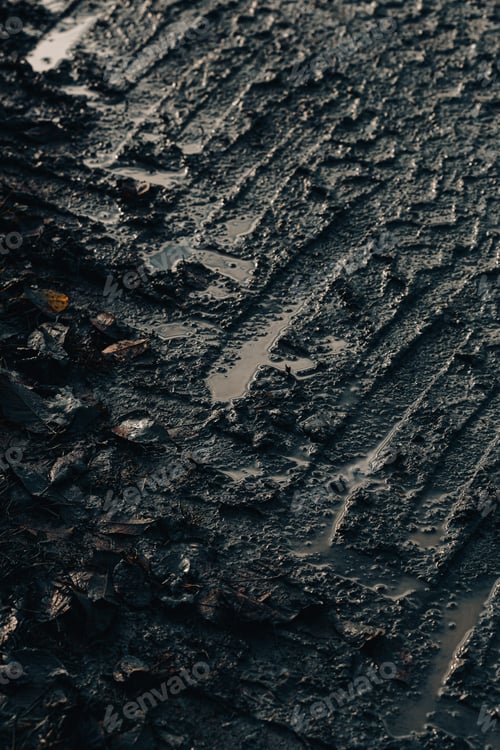 Preview: dark muddy road background with tire traces, dirty ground and autumn leaves