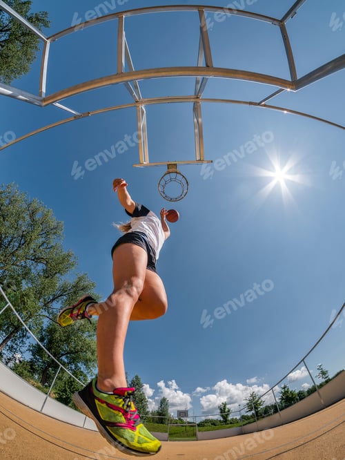 Preview: Young woman playing basketball against the sun